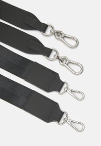 Cinghie nere realizzate in nylon e pelle presentano clip e accessori metallici di colore argento, con una texture liscia e dettagli rettangolari.