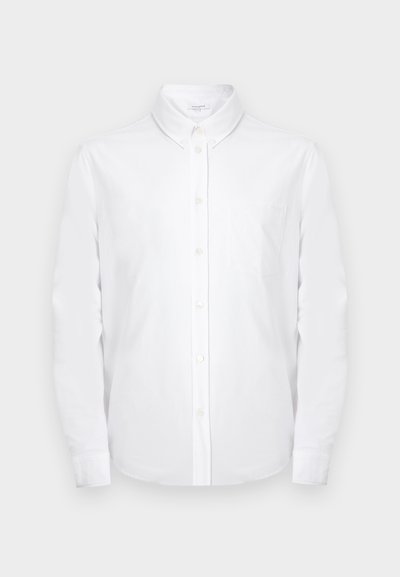 Λευκό πουκάμισο με μακριά μανίκια και κουμπιά, με μυτερό γιακά και τσέπη στο στήθος, σε απλό ανοιχτό γκρι φόντο.