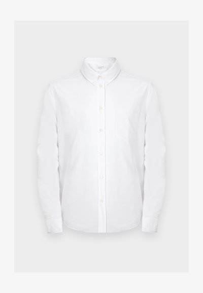 Λευκό πουκάμισο με μακριά μανίκια και κουμπιά, με μυτερό γιακά και τσέπη στο στήθος, σε απλό ανοιχτό γκρι φόντο.