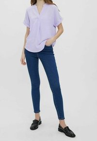 Blouse à manches courtes de couleur violet clair avec un col en V, associée à un jean skinny bleu foncé et des mocassins noirs, présentant une tenue décontractée.