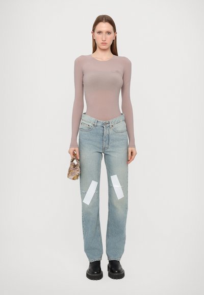 Langärmliger, hellmaulbeerfarbener Bodysuit; verwaschene blaue Jeans mit weißen Flecken; schwarze Plateaustiefel; kleine Handtasche mit Muster. Einheitlicher Hintergrund.
