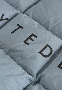 Tissu matelassé bleu clair avec des sections rectangulaires et des lettres noires en gras. Le matériau semble doux avec une texture légèrement brillante.