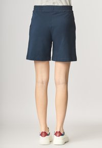 Pantaloni corti blu navy con vita elastica, texture liscia e tasche laterali. Indossati con sneakers bianche con accenti rossi e blu.