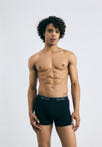 Boxeri negri din bumbac cu un brâu contrastant ce prezintă logo-ul "Calvin Klein". Modelul are părul creț și o constitutie musculară.