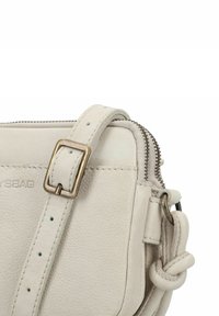 Borsa a tracolla in pelle di un morbido grigio chiaro con una finitura testurizzata. Presenta una chiusura con zip, una tracolla regolabile e accenti in ottone.