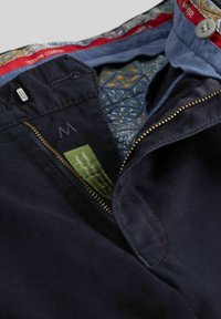 Pantalons navy avec une fermeture éclair et un accent en métal, présentant une doublure à motifs colorés et une étiquette en tissu vert indiquant un matériau organique.