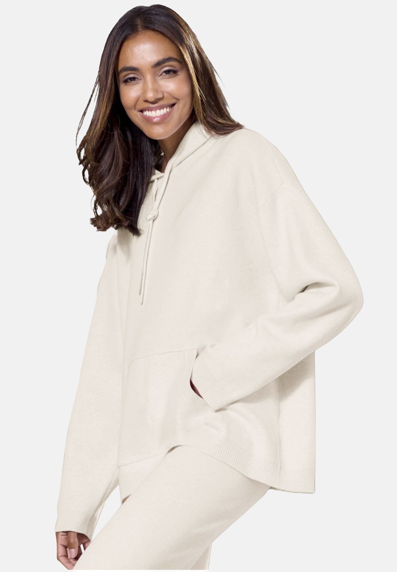 Bež velika kapuca s vezicami, sprednjim žepom, rebrastimi manšetami in robom. Mehka tkanina in sproščen kroj za udobje.