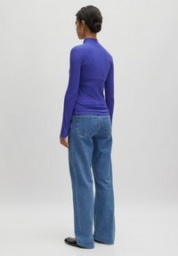 Langarmige geribbelde top in levendig paars, gecombineerd met hoogopgesneden, loszittende blauwe denim jeans. Zwarte flats maken de look compleet.