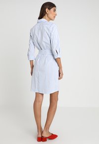 Vestito a camicia a righe in azzurro chiaro e bianco, con maniche three-quarter, una cintura a fusciacca e un taglio sartoriale che arriva sopra il ginocchio.