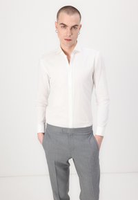 Weißes langärmliges Button-Down-Hemd aus glattem Stoff, ergänzt durch graue, taillierte Hosen mit subtilen Mustern und Seitentaschen.