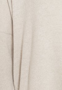 Beiger, strukturierter Stoff, der teilweise drapiert ist, mit einem weichen, gestrickten Design und subtilen Farbvariationen. Keine deutlichen Muster oder Hardware sichtbar.