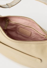Μπεζ δερμάτινη τσάντα με υφή στην εξωτερική επιφάνεια και χρυσό φερμουάρ. Η εσωτερική επένδυση είναι ροζ με ετικέτα λογότυπου και επιπλέον τσέπη με φερμουάρ.