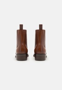 Botas de tobillo de cuero marrón con paneles laterales elásticos, lengüetas y un ligero tacón, con una textura suave y líneas limpias.