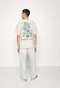Cream cotton T-shirt with a large green dragon and floral print on the back. Relaxed fit, paired with light blue wide-leg jeans.