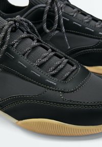 Baskets noires avec des lacets noirs et blancs texturés, tige en cuir et tissu cousu, et semelles en caoutchouc texturé marron clair.