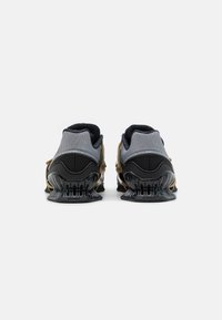 Scarpe da ginnastica nere e grigie con una tomaia in rete testurizzata, dettagli dorati e un distintivo design della suola nera ondulata.