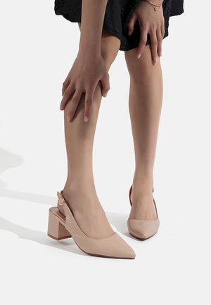 Tacchi slingback beige con punta affusolata, tacco a blocco e chiusura con fibbia laterale. Finitura in pelle verniciata liscia e dettagli di cucitura minimi.