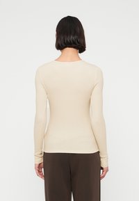 Πουκάμισο μακρυμάνικο σε εφαρμοστή γραμμή από απαλό μπεζ ύφασμα με ρίγες, με στρογγυλεμένη λαιμόκοψη και εφαρμοστά μανίκια, σε συνδυασμό με παντελόνι σκούρου  καφέ.