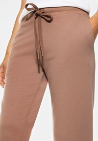Pantalons de survêtement en coton brun avec une taille élastique, dotés d'un cordon de serrage et de poches latérales. Texture lisse, coupe fuselée.