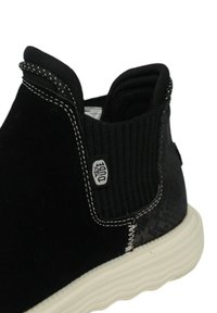 Stivale alla caviglia in suede nero con pannello elastico laterale, suola in gomma bianca, cuciture a contrasto e un motivo decorativo sul tacco.