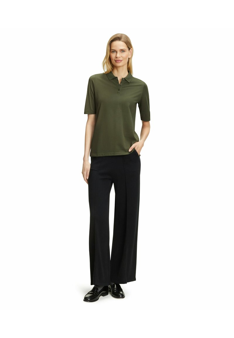 Olijfgroene poloshirt met korte mouwen, voorzien van een knoopsluiting kraag, gecombineerd met wijde zwarte broek en zwarte schoenen.