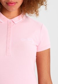 Jasnoróżowa koszulka polo wykonana z teksturowanej tkaniny, wyposażona w klasyczny kołnierzyk, zapięcie na guziki oraz białe wyszywane logo na piersi.