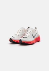 Nike futócipők, fehér textil felsőrésszel, fekete részletekkel, hangsúlyos piros középtalppal és textúrázott fekete gumitalppal.