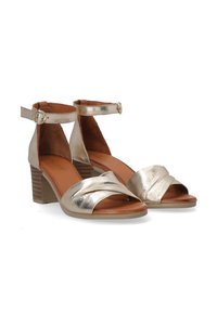 Goldene metallische Absatzsandalen mit überkreuzten Vorderträgern, einem Knöchelriemen mit Schnalle und einem gestapelten Blockabsatz. Weiche Innenauskleidung.