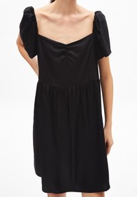 Černé šaty s nabíranými rukávy, hranatým výstřihem, zdobené na předním dílu a s rozšiřující se sukní. Vyrobeny z měkké, lehké látky.