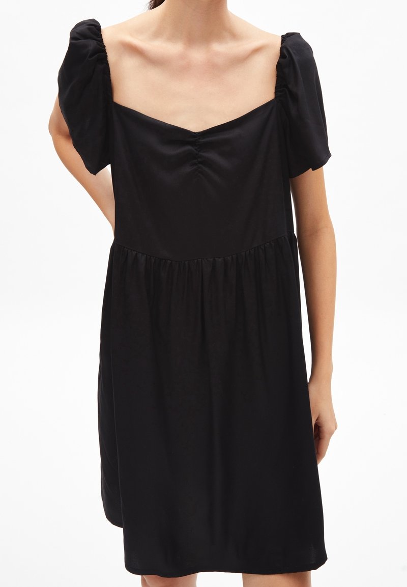 Černé šaty s nabíranými rukávy, hranatým výstřihem, zdobené na předním dílu a s rozšiřující se sukní. Vyrobeny z měkké, lehké látky.