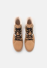 Stivaletti alla caviglia color suede beige con un morbido colletto in pelliccia bianca, lacci neri, dettagli in oro e cuciture a contrasto. Suola piatta e punta tonda.