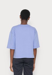 T-shirt in cotone azzurro, a maniche corte e vestibilità morbida, con scollo a girocollo e orlo arrotondato. Abbinato a pantaloni neri a righe sottili.