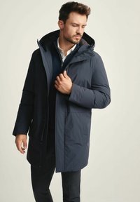 Granatowa kurtka puchowa z kapturem, z zamkiem błyskawicznym z przodu i bocznymi kieszeniami. Gładka tekstura z subtelnymi detalami w szwie oraz luźny krój.