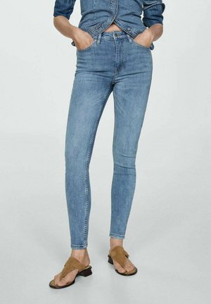 Světle modré džíny skinny s vysokým pasem, které mají pět kapes a klasické zapínání na knoflík, v kombinaci s hnědými plochými sandály.
