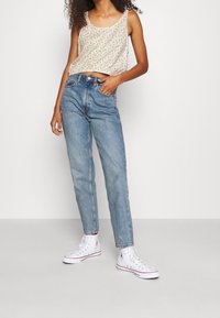 Top sin mangas de flores en crema, jeans de tiro alto de color azul claro y zapatillas de lona blancas con acentos rojos. Diseño de atuendo sencillo y casual.