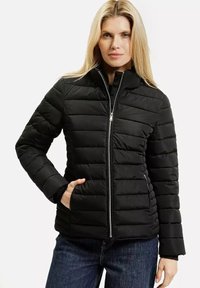 Czarna kurtka puchowa z wysokim kołnierzem, poziomym pikowaniem, zamek błyskawiczny oraz bocznymi kieszeniami. Noszona na ciemną bluzkę i dżinsy.