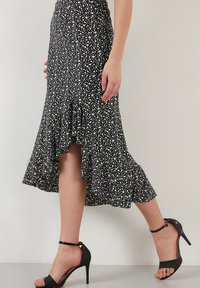 Fustă midi cu imprimeu floral alb-negru, cu o margine franjurată, având talia ajustată și o formă fluidă. Asortată cu sandale negre cu toc înalt.