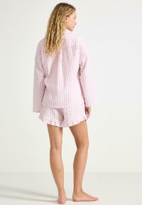 Rosa gingham pyjamaset med långärmad skjorta och volangshorts. Texturerat tyg med rutmönster, med knäppt front.