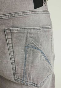 Lysegrå denimjeans med en s�ærpræget baglomme, der har blå syninger og struktureret stof. Sort lædermærke nær taljen.