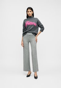 Γκρι πουλόβερ με ροζ γράμματα "Futuro", συνδυασμένο με γκρι παντελόνες ψηλόμεσες και φαρδιές. Το μοντέλο φοράει μαύρα mule με τακούνι.