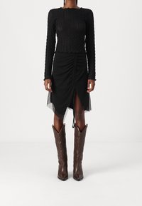 Svart stickad långärmad topp med strukturerat mönster, i kombination med en höga midjan svart rynkad kjol med genomskinliga inslag och bruna läder knähöga stövlar.