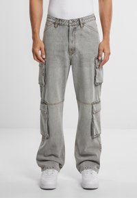 Pantaloni cargo grigio chiaro caratterizzati da tasche oversize, una vestibilità rilassata, cuciture visibili e un taglio a gamba dritta abbinati a sneakers bianche.