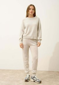 Jasnoszary sweter dzianinowy i dopasowane joggery z prążkowanymi mankietami. Miękka tekstura i luźny krój, w połączeniu z białymi i szarymi sneakerami.