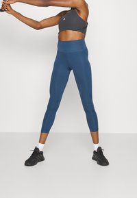 Sportbh i mörkgrått med racerback-design och högmidjade, teal leggings. Leggingsen har en slät textur och en figursydd siluett.