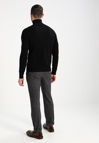 Un pull à col roulé noir associé à un pantalon texturé gris et des chaussures marron, présentant une coupe slim et un design épuré.