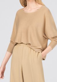 Jasnobeżowy, oversize sweter z okrągłym dekoltem i ściągaczami, zestawiony z pasującymi, beżowymi spodniami plisowanymi. Miękka, gładka tekstura.