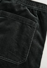 Black corduroy pants feature vertical ribbing, an elastic waistband, and a single back pocket. The fabric has a soft texture.