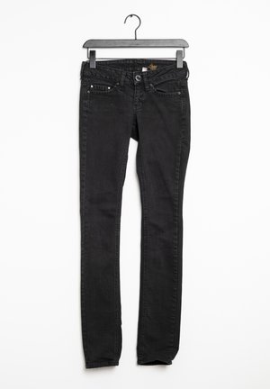 Jeans en denim noir avec une coupe slim, comportant cinq poches, une fermeture éclair et des détails de couture subtils. Suspendus sur un cintre en plastique noir.