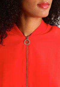 Röd tröja med dragkedja och rund metallisk dragkedjekontakt samt ribbad krage. Mjuk textur och figursydd design som framhäver ett elegant utseende.