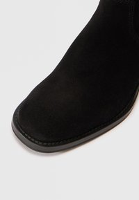 Stivale alla caviglia in suede nero con punta arrotondata, dettagli cuciti lungo il bordo e suola in gomma nera lucida.